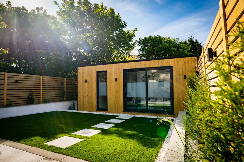 Landscaped courtyard with stepping stones across an artificial lawn leading to a garden room with sliding doors and wall lights