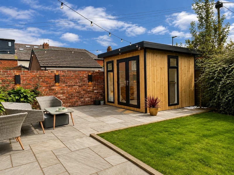 Redwood garden room with French doors and a side window, opening onto a paved seating area with festoon lights strung above