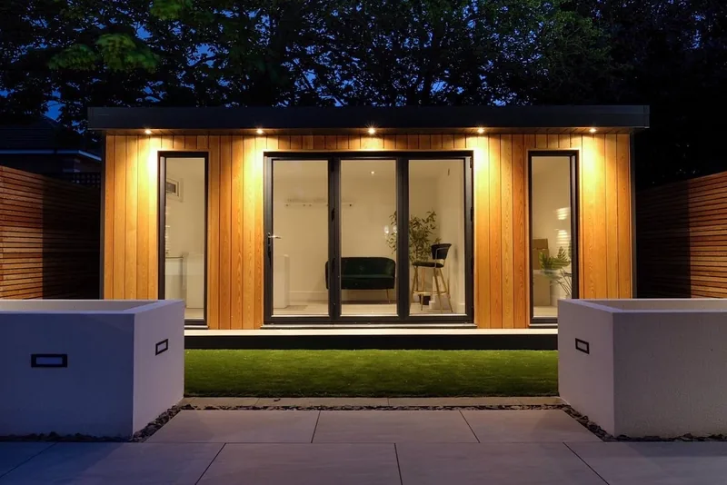 Cedar garden room at dusk, downlights along the fascia and rendered planters on the terrace in front of it