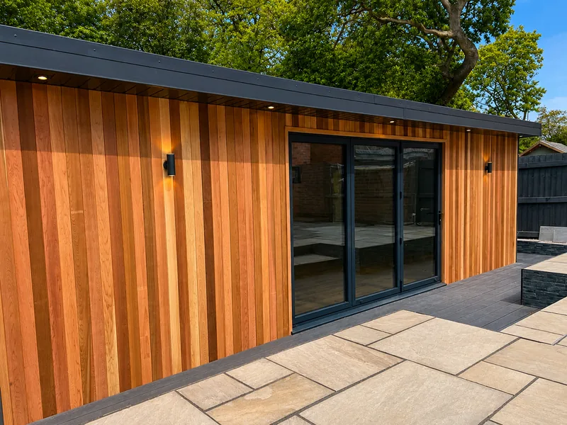 Long cedar elevation with a dark sliding door, running away down a sandstone patio in low afternoon sun