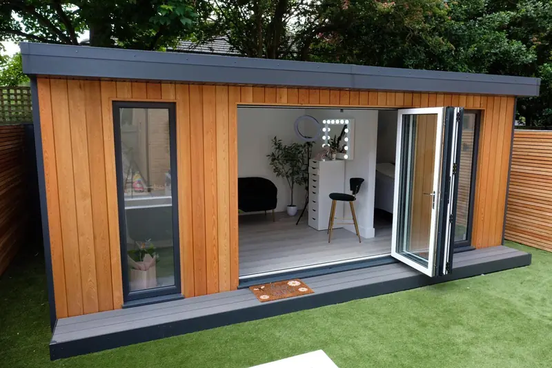 Garden beauty studio with vertical cedar cladding and white bi-fold doors opening to a dressing table and mirror lights