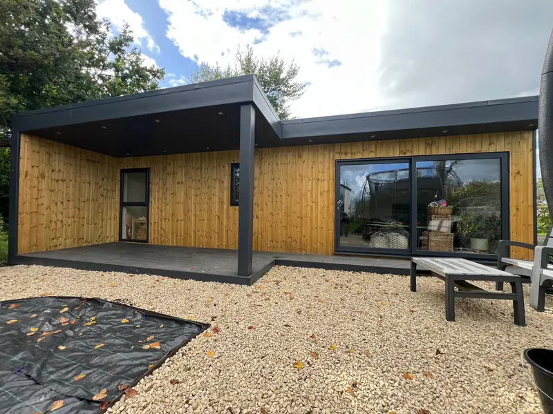 Garden room with a large covered canopy over decking, pale vertical redwood cladding and grey sliding doors