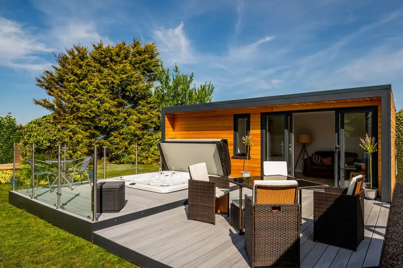 Garden retreat with a hot tub and rattan furniture on tiered composite decking behind a glass balustrade