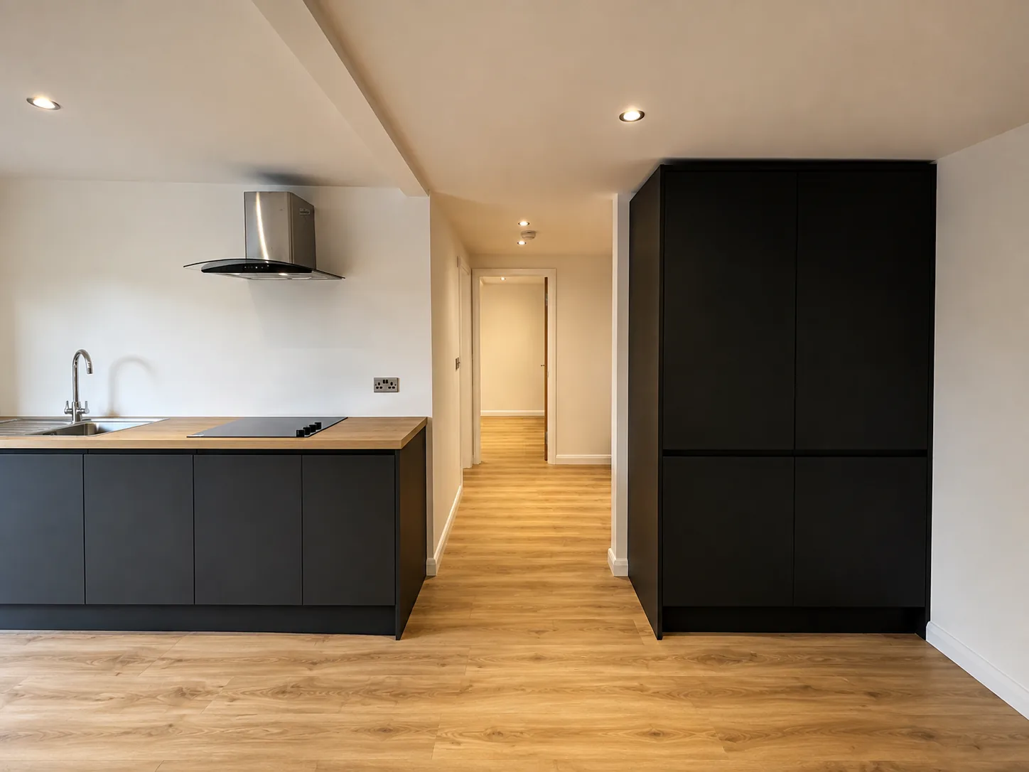Fitted kitchen inside a garden annexe: dark handleless units, an extractor over the hob and oak flooring running through to the hall