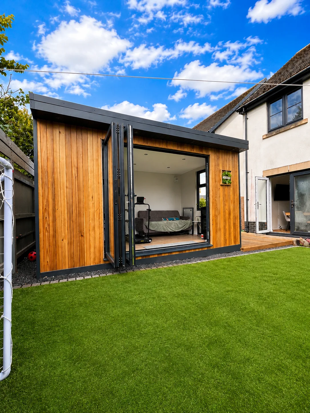 Cedar garden room with its bi-fold doors folded right back onto the lawn beside the house, the room visible inside