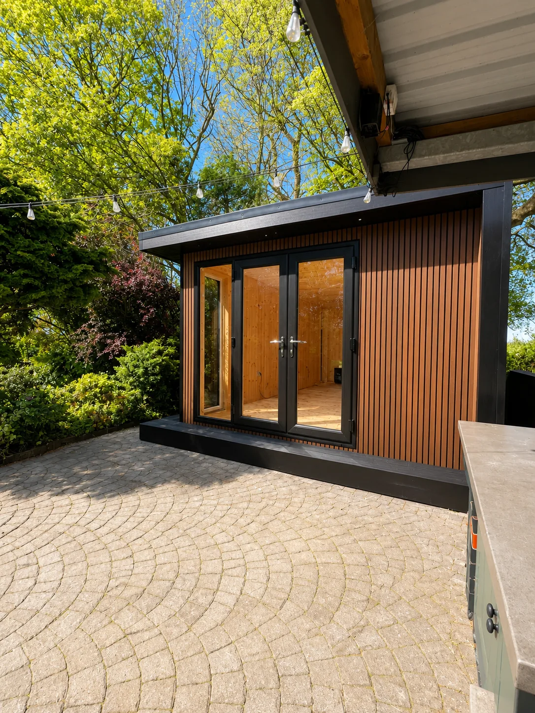 Cedar garden room with French doors opening onto cobbled paving, planting either side and a canopy overhead